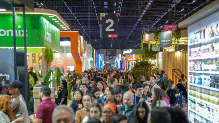 orredor movimentado da NaturalTech e Bio Brazil Fair 2025, com centenas de visitantes circulando entre estandes de diferentes marcas do setor de alimentos, nutrição, suplementos e produtos naturais. Ambiente iluminado e vibrante, com destaque para a variedade de empresas expositoras.
