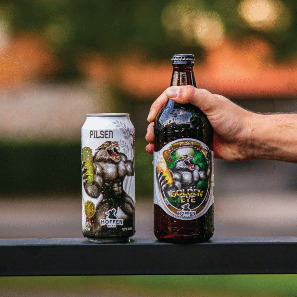 Rótulos e sleeve ilustrados da cerveja Hoffen Golden Eye Pilsen em garrafa e lata com design de lobisomem musculoso.